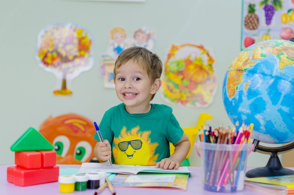 Boy in kindergarten drawing at school whilst smiling