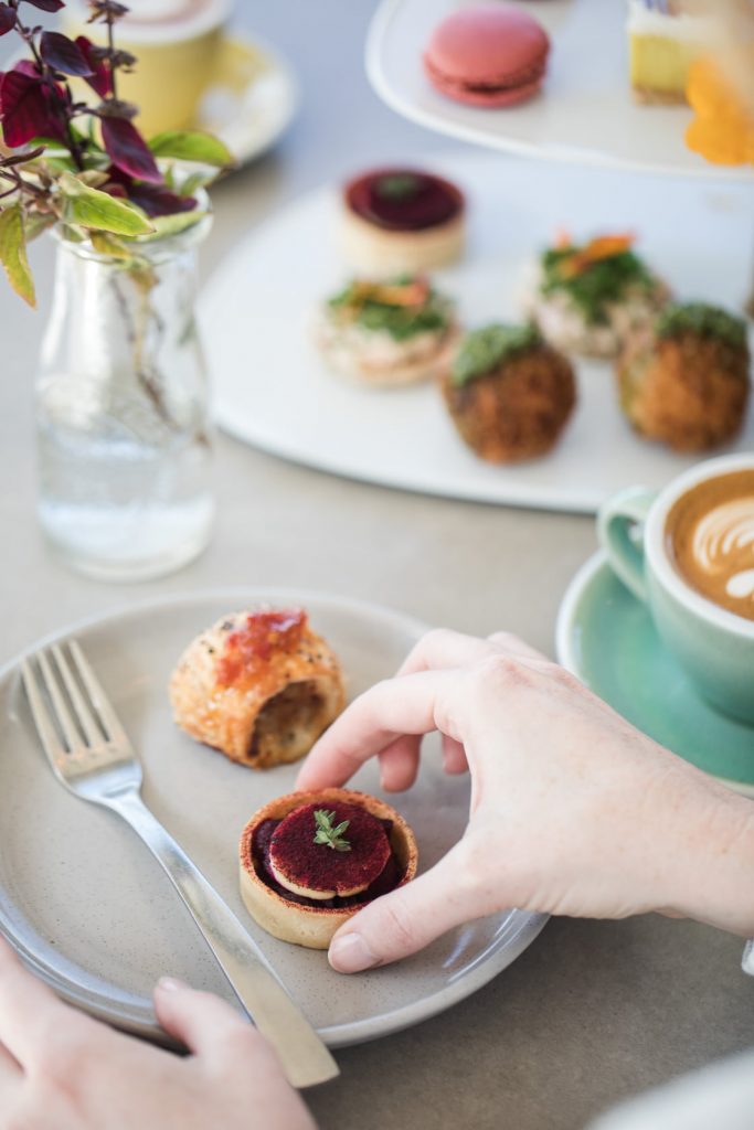 Hand taking a small treat from a plate in a Cafe in Perth offering High tea